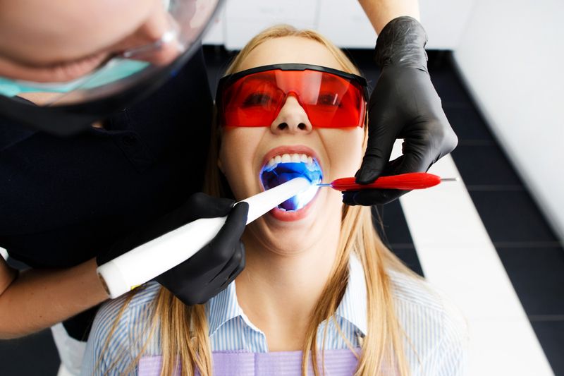 women opens her mouth and dentist doing teeth bleaching operation with equipments